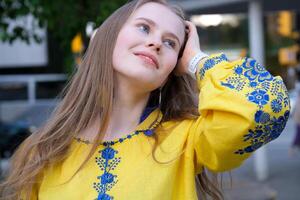 young beautiful woman, young girl in big city in yellow embroidered shirt, embroidered blouse, long brown hair, smile, feather earrings, yellow and blue colors in clothes, Ukrainian national costume photo