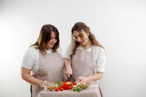 mujer madre y hija preparando ensalada mamá hija cortes rojo campana pimienta idéntico cocina delantales espacio para texto enseñando Cocinando colegio casa delicioso comida Fruta y vegetal Tienda tienda de comestibles foto