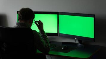 close-up green screens of two monitors man in dark sits with back ad optics space for text online training computer programs fatigue rest time to travel soon weekend working days office weekdays photo