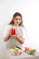 Smiling brunette woman holding red bell pepper while standing with hand on hip Green vegan salad with mixed green leaves and vegetables Green salad with tomatoes and fresh vegetables photo