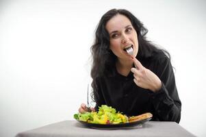 a woman eats a piece of meat carefully chew food close-up face of a beautiful light-eyed black-haired middle-aged woman on a white background photo