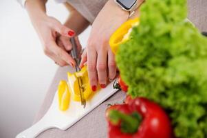 adult teaches child to cut vegetables mother helps son to cut yellow bell pepper close-up hands knife and porcelain whiteboard healthy vegetables first steps in cooking training photo