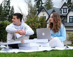 A young girl and a boy look away with a slice of pizza and a laptop in their hands on the street, satisfied they waited for the food to be delivered. Very tasty Good time with friends photo