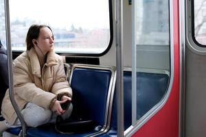 vancouver canada listen to music on headphones go home to study Teen girl looking at window of metro train. Cute woman travel by sky train Concept of public transport and urban journey photo