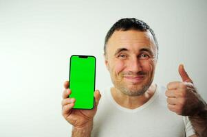 positivo milenario hombre demostración enorme marca nuevo teléfono inteligente con vacío pantalla y pulgar arriba terminado blanco estudio fondo, Bosquejo, panorama con Copiar espacio, el más nuevo móvil aplicación concepto foto