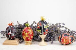 Easter holiday banner white background for text advertising Postcard lavender flowers next to the eggs painted painted eggs on wooden stands four multi-colored eggs Ukrainian flavor black red green photo