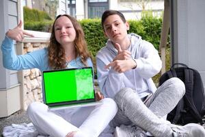 green screen chroma key teenagers study online sitting on the street with a laptop Girl and boy outdoor. Freelancer communicate on project, shopping online on wifi tablet. Working business process photo