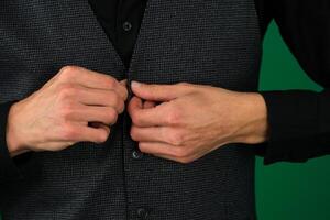 close-up photo of the hands of a man in a black shirt, buttoning up a button on green background