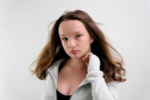 bien arreglado marrón pelo hermosa joven niña adolescencia ondulación su cabeza lento movimiento en un blanco antecedentes estudio ajustar su chaqueta apoyarse a el lado sonrisa sensibilidad belleza foto