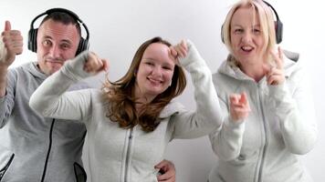 alegre familia en auriculares bailando demostración pulgares arriba en contra el antecedentes de blanco chándales teniendo divertido familia Deportes gasto hora juntos contento familia mamá hija padre alegre música foto