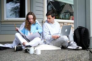 Study and technology laptop large folder with files sit on plaid next to cup and briefcase Young man and woman holding smartphone and reading book Student studying for exam,using mobile phone in park. photo