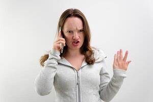 Surprised and angry woman speaking on cellphone on blue shirt standing over white background photo