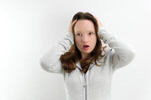 Screaming angry young woman holding her head between hands. horror open your mouth in surprise open your eyes wide hold your head with your hands on a white background teenager great surprise photo