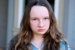 Young beautiful very angry teenager girl with brown wavy hair looking directly at camera with strict facial expression. outdoor studio shot isolated on gray background. photo