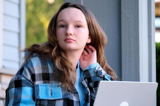 Beautiful woman chatting on mobile phone while sitting with portable laptop computer on campus, young female in good mood reading text message on cell telephone while resting after work on net-book photo