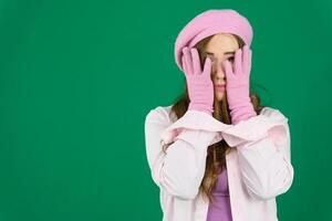suffering experiences sadness girl with two hands wearing knitted pink gloves covers her face on a green background chromakey failed expectations boredom cold autumn winter photo
