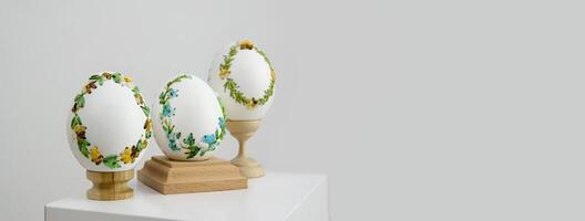 three eggs on special wooden stands on a white background lavender background postcard baner calendar empty space holiday easter eggs embroidery ribbons on eggshell krashanka photo