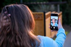 joven mujer de el latín carrera con rubia pelo tomando un foto a puesta de sol a compartir eso en social redes en un parque en primavera día.