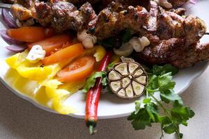 Shashlik or shish kebab prepared on barbecue grill over hot charcoal with grilled vegetables. Grilled pieces of pork meat on metal skewers. photo
