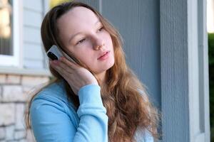 Beautiful woman chatting on mobile phone while sitting with portable laptop computer on campus, young female in good mood reading text message on cell telephone while resting after work on net-book photo