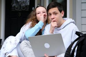 Shocked couple friends girl in white casual clothes whispering secret behind hand while sharing news teenagers gossip communicate sitting with a laptop on porch of house with briefcase under blanke photo