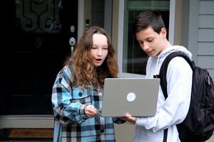 boy shows something on laptop of girl she corrects mistakes she smiles a briefcase loser first relationship boy teenager clothes autumn spring near the house at door to come to friend to help photo
