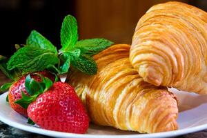 on a plate two delicious appetizing fresh croissants with strawberries and mint appetizing food purchases Grocery wheat flour butter advertisement of any product related to leisure and food place photo