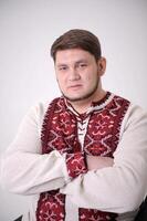 adult handsome man in a white embroidered shirt he crossed arms over chest he has blue eyes thin beard he is against white background of village of courage Bogatyr Ukrainian people symbols of Ukraine photo