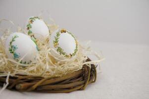 Easter three beautiful embroidered eggs with eggshell ribbons in a nest with wrapping paper white background space for text congratulations meeting with family decoration home decoration gift delivery photo