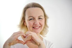 woman sincerely smiles with her hands shows a heart squinting her eyes on a white background love feelings joy valentine's day like goods product delivery advertising space we I love it love you photo