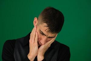 emotions of a handsome man guy on a green background chromakey close-up dark hair young man Tired men. Portrait of tired young men holding his hands on face while photo