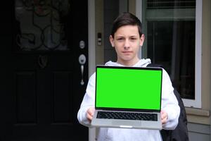 Amazed excited caucasian young man peeking out from behind laptop, looks surprised at camera, stands on isolated white background, holds an open laptop with blank white screen, copy space, mock-up photo