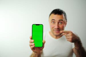 Positive millennial man showing huge brand new smartphone with empty screen and thumb up over white studio background, mockup, panorama with copy space, newest mobile app concept photo