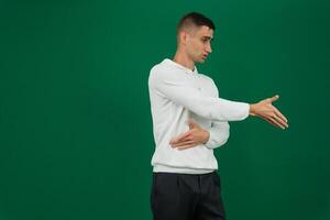 hand shake man a young guy in a white sweatshirt and black jeans on a green chromakey background offers his hand to shake, turn to the left photo