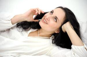 Top view of beautiful brunette woman lying on white silk bed using smartphone photo