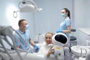 middle-aged woman in dental chair shows tongue and laughs she hides behind soft toy white astronaut in background doctor and nurse look latest technology fun joy pleasure in dentist's office photo