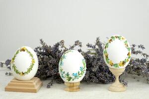 three eggs on special wooden stands on a white background lavender background postcard baner calendar empty space holiday easter eggs embroidery ribbons on eggshell krashanka photo