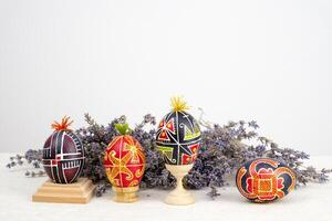 Easter holiday banner white background for text advertising Postcard lavender flowers next to the eggs painted painted eggs on wooden stands four multi-colored eggs Ukrainian flavor black red green photo