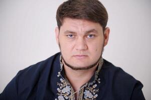 strong confident look of blue eyes of man in blue shirt with embroidery in front frowning forehead moving eyebrows who opened cancer eyes thin beard narrow lips concept of power of confidence photo