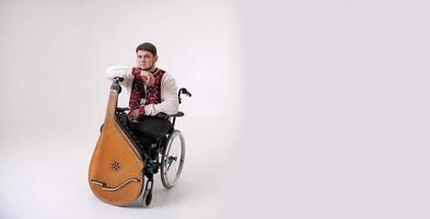 banner young man with kobza musical instrument in hands sits on white background on wheelchair without legs war veteran dressed in Ukrainian embroidered shirt national symbols of Ukraine vyshyvanka photo