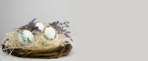 easter holiday banner side view of eggs in nest with lavender flowers ribbon embroidery on eggshell white eggs lie on straw on right space for text advertising ads postcard billboard easter holiday photo