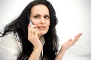 dissatisfied brunette talking on the phone she shows her hand to the side wrinkle her forehead displeasure horror sad face unpleasant conversation negative emotions photo