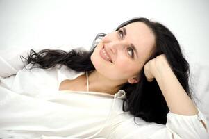 middle-aged woman lying on the bed adjusting her hair white nightgown nightgown blue eyes black hair red nails manicure personal care Tenderness trying to lie down comfortably natural beauty photo