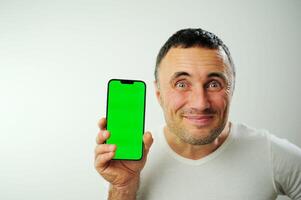 positivo milenario hombre demostración enorme marca nuevo teléfono inteligente con vacío pantalla y pulgar arriba terminado blanco estudio fondo, Bosquejo, panorama con Copiar espacio, el más nuevo móvil aplicación concepto foto