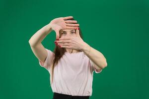 retrato de sonriente joven mujer haciendo un mano marco diferente emociones de un joven niña en un verde antecedentes chromakey hermosa facial caracteristicas real personas rosado camiseta blanco desollado europeo. negro foto