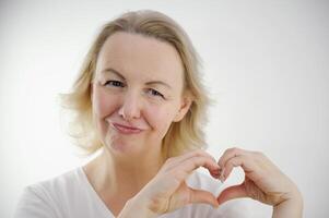 hacer manos corazón de edad mediana mujer confiesa amor en San Valentín día participación labios sonriente inclinación cabeza demostración un corazón con manos diciendo me gusta esta labios estirado fuera dentro tubo cebolla astuto en amor Mira foto