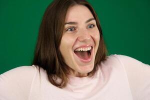 Happy young girl smiling cheerfully holding hands in front of her. Isolated different emotions of a young girl on a green background chromakey beautiful facial features real people pink T-shirt white photo