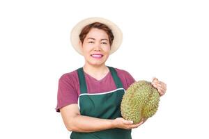 Happy Asian woman wears hat, green apron, holds durian fruit. White background. Concept, fruit seller, gardener occupation. Durians,seasonal fruits and popular. photo