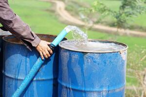 Close up farmer hand hold pipe of water to put into blue buckets in garden. Concept, Solve problems lacking of water in agriculture by prepare water for watering plants in drought season. photo