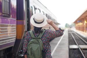 Back view of female traveller, wear white hat and backpack, go travelling by train at local railway station in Thailand. Concept, lifestyle. Journey, travelling Tourism. photo